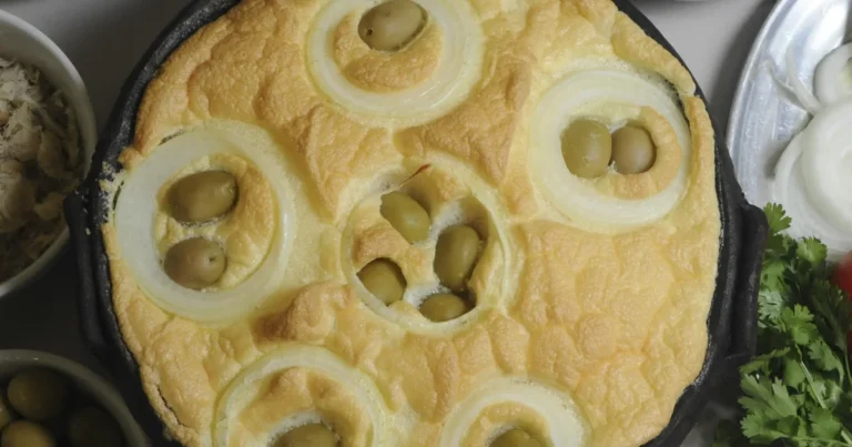 Torta capixaba assada em panela de barro, com cobertura dourada de clara em neve, rodelas de cebola e azeitonas, acompanhamentos ao redor