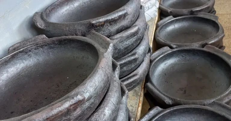 Panelas de barro pretas de Goiabeiras empilhadas, com assadeiras ovais e panelas de caldo à mostra