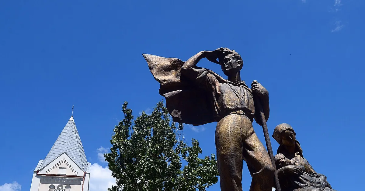 Escultura de bronze de um casal de imigrantes com enxada e trouxa, com a torre da igreja luterana atrás