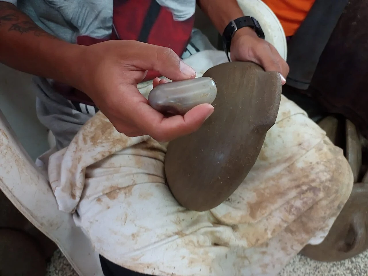 Mãos alisando com seixo uma peça de barro crua no ofício das paneleiras de Goiabeiras