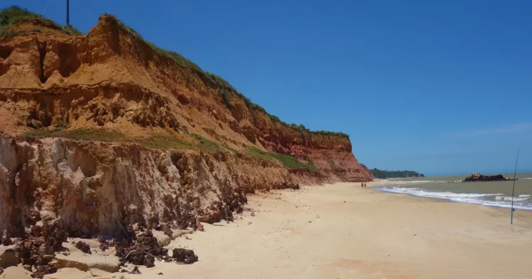 Falésias coloridas de Marataízes - ES, com paredões em tons de laranja e vermelho ao lado da faixa de areia
