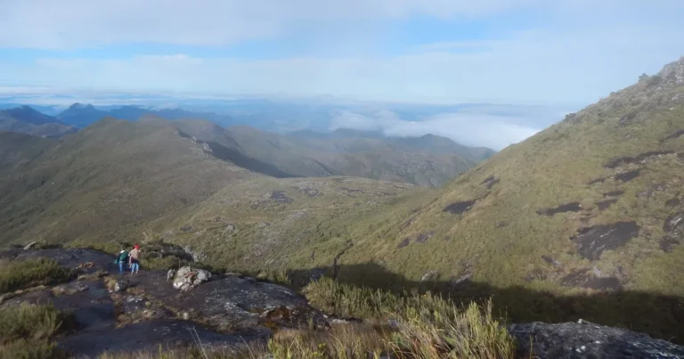 Trilha do Pico da Bandeira pelo lado capixaba, com caminhantes no leito de pedra e mar de nuvens sobre a serra