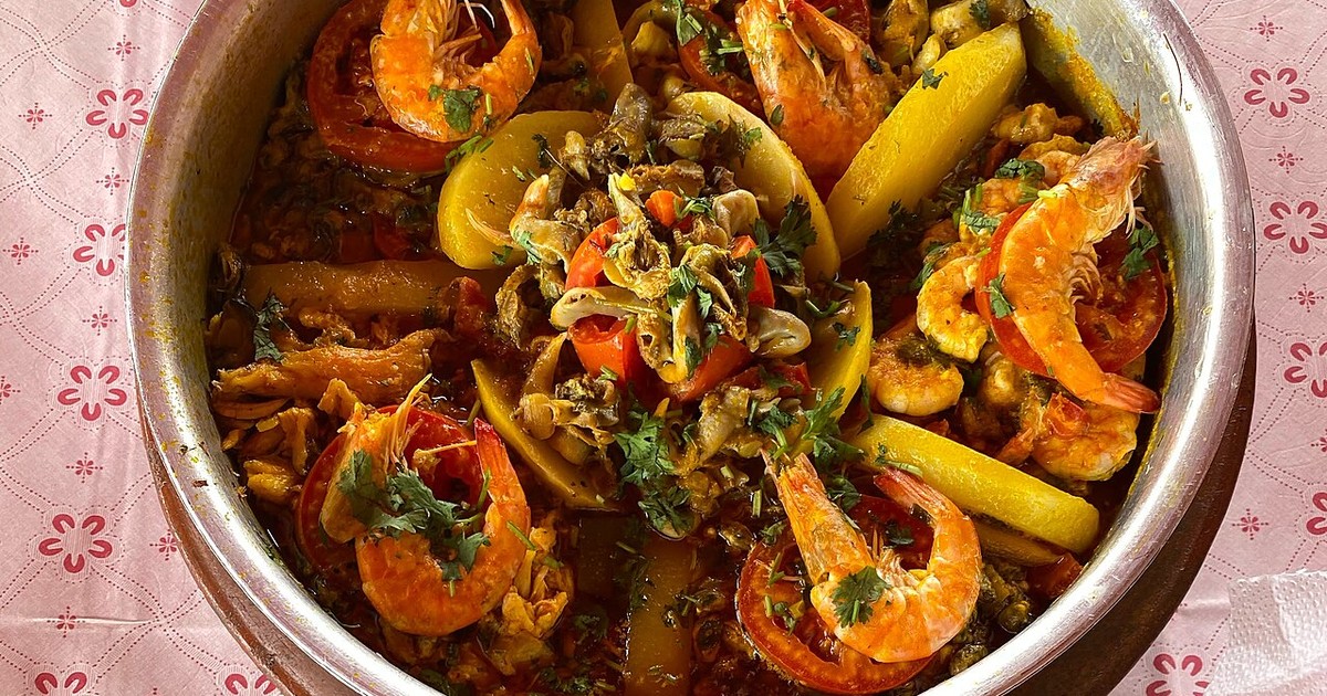 Panela de moqueca baiana com postas de peixe, camarões, rodelas de tomate e coentro no caldo amarelo de dendê