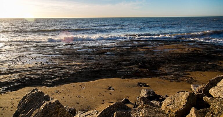 Faixa de areia e plataforma de arenito exposta na maré baixa em uma praia de Marataízes, no fim da tarde