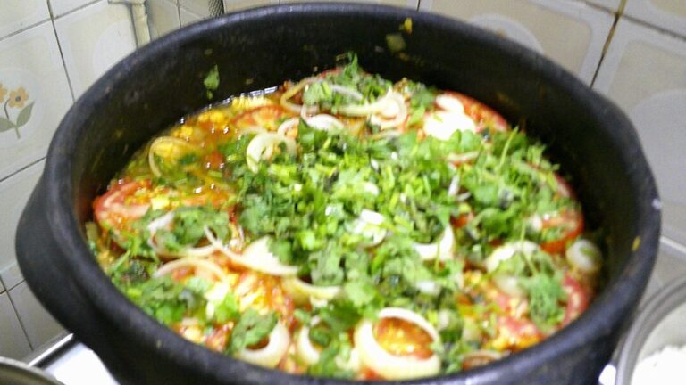 Moqueca capixaba com tomate, cebola e coentro sobre o peixe, dentro de uma panela de barro preta