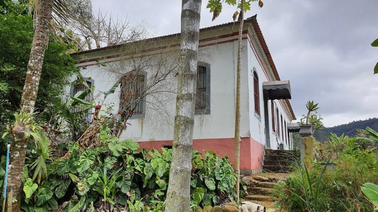 Casa-sede de fazenda em Santa Leopoldina (ES), de paredes brancas e barrado vermelho, cercada de vegetação