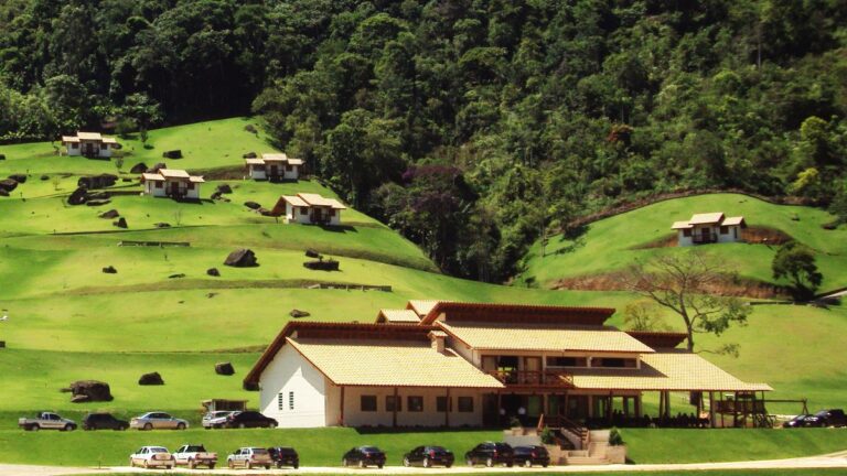 Chales espalhados por encosta gramada e predio principal de hospedagem, com mata ao fundo, em Venda Nova do Imigrante (ES)