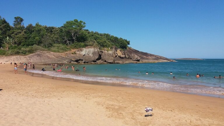 Enseada curta da Praia dos Padres, em Guarapari, com costão de rocha coberto de vegetação e mar raso na faixa de areia