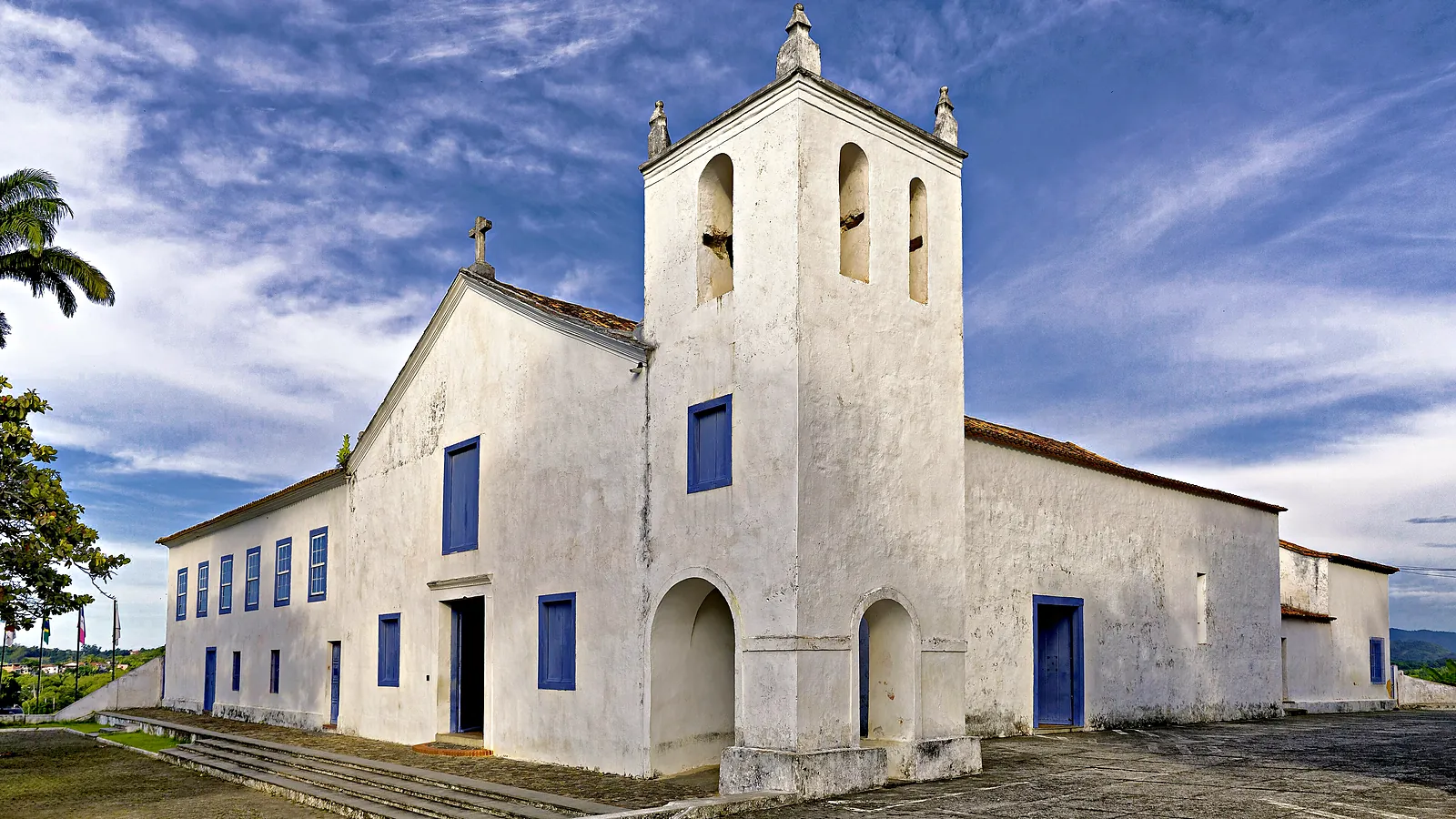 Fachada branca do Santuário Nacional de São José de Anchieta, em Anchieta (ES), com a torre do sino e o adro de pedra sob céu azul
