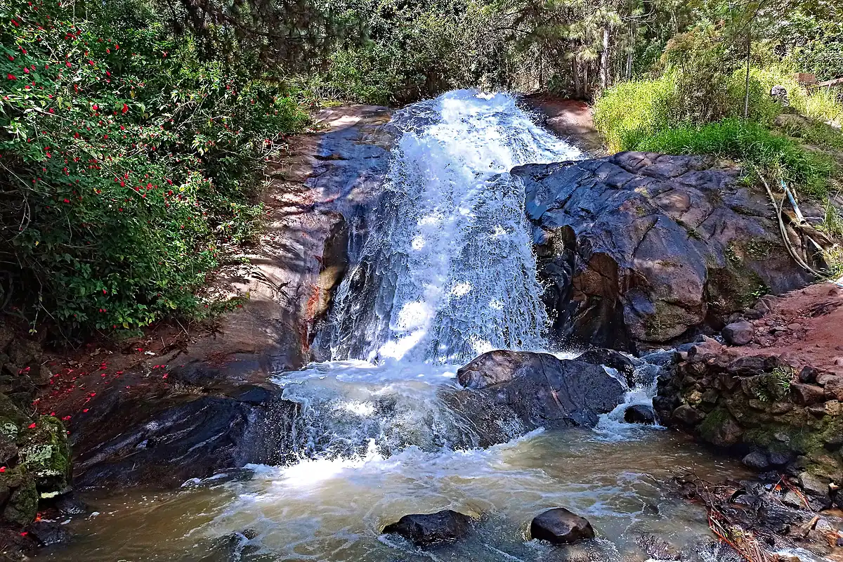 Cachoeira da Bica, em Marechal Floriano (ES), com a água descendo entre pedras escuras e mata em volta, até um poço raso de águas agitadas