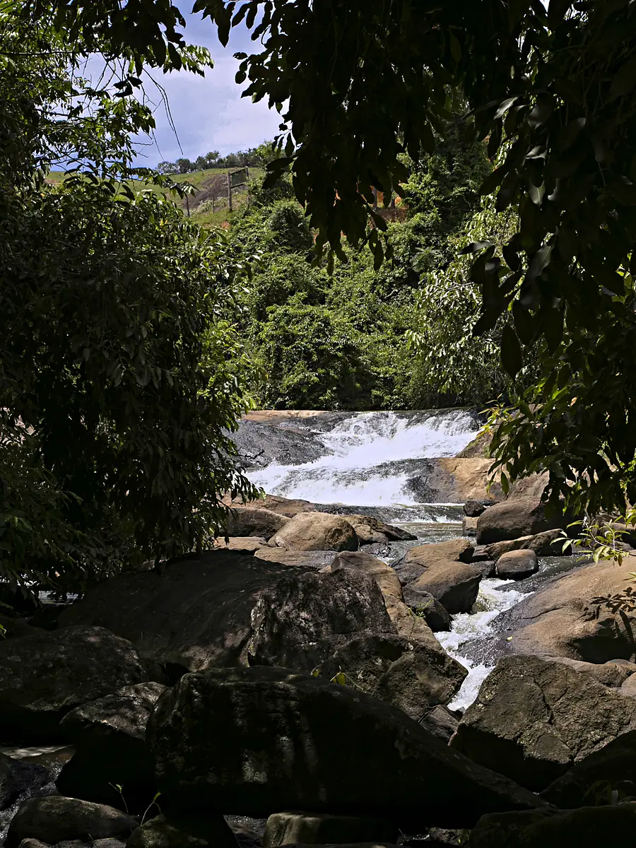 Corredeira da Cachoeira De Angeli, em Linhares (ES), vista entre árvores, com a água branca descendo sobre pedras grandes
