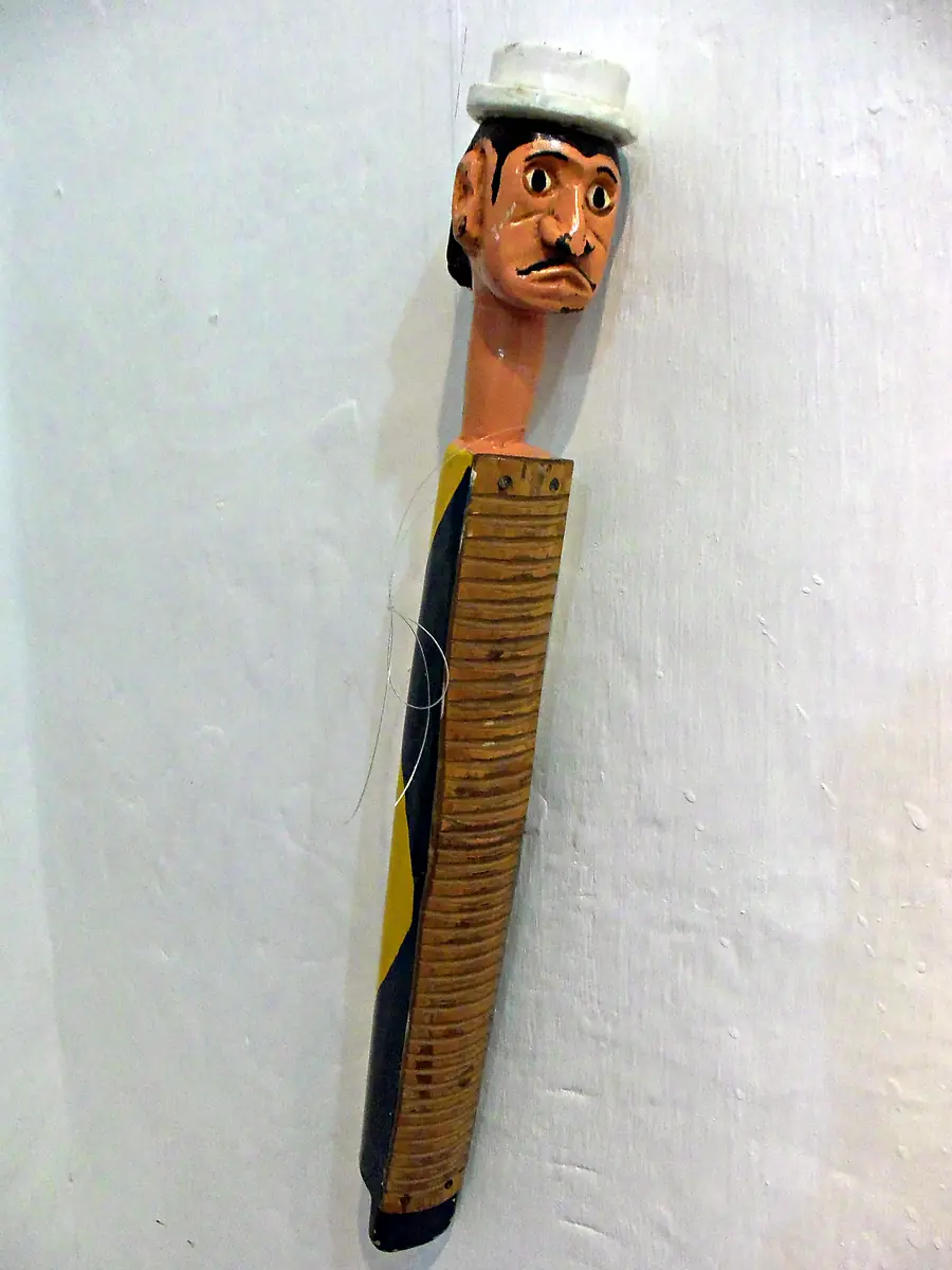 Casaca com cabeça esculpida de bigode e chapéu branco e costela de bambu em talhos, encostada numa parede branca da Igreja dos Reis Magos, em Nova Almeida, na Serra (ES)