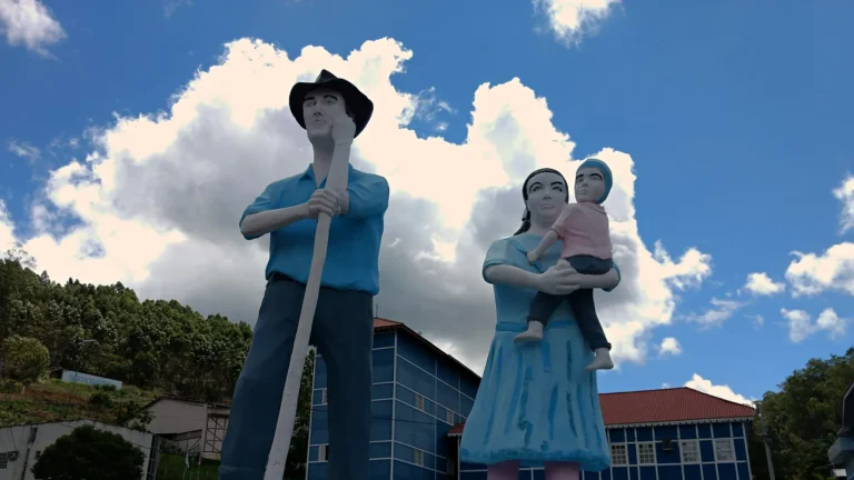 Estátuas de um casal de colonos pomeranos com uma criança no colo, sob céu azul, diante dos prédios azuis da Câmara Municipal de Santa Maria de Jetibá