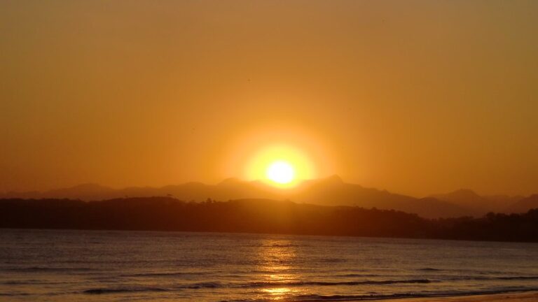 Pôr do sol com céu limpo sobre o mar em Anchieta - ES, com o reflexo do sol na areia molhada